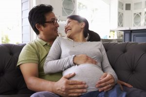 Expectant Couple Relaxing On Sofa At Home Together