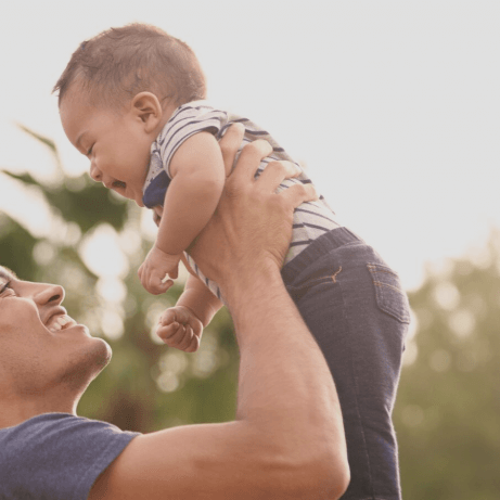 Millennial Hispanic father holding his little baby in the air in the park, close up