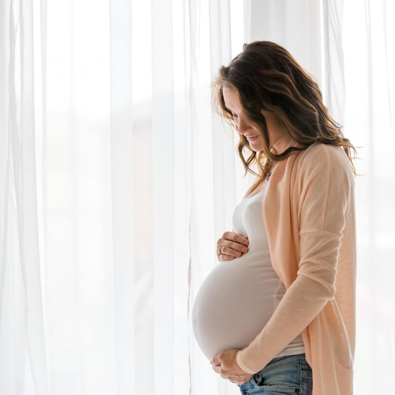 Portrait of young pregnant attractive woman, standing by the window